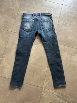 Mörkblå slim fit jeans med slitningar - Säljer ett par mörkblå slim fit jeans med snygga slitningar och tvättade detaljer på framsidan. Jeansen har klassisk femficksmodell och raka ben. Perfekta för en avslappnad och trendig look. Storlek 31/32