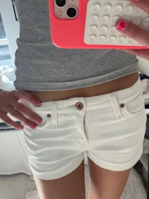 Vita denimshorts från Lee - Snygga vita denimshorts från Lee med klassisk femficksdesign och bruna detaljer vid knappar och nitar. Shortsen har låg midja och är perfekta för varma dagar. Styla med en crop top eller oversized t-shirt för en chill look. Står ingen storlek men skulle säga att dem är som xs/s