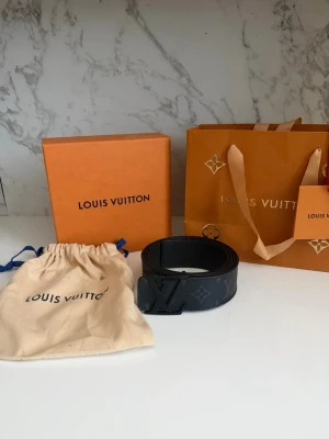 Louis Vuitton Monogram Shadow-bälte – Svart  - Säljer mitt Louis Vuitton Monogram Shadow-bälte i svart. Bältet är i gott skick och säljs som ett komplett set, inklusive:  Original Louis Vuitton-box Original dammpåse (dust bag) Originalförpackning  Bältet har det diskreta Monogram Shadow-mönstret präglat i lädret, vilket ger en stilren och exklusiv look som passar både till vardags och mer uppklädda tillfällen.  Skick:  Bra övergripande skick med normala tecken på användning. Ett extra hål har gjorts av mig för att ge en bättre pass