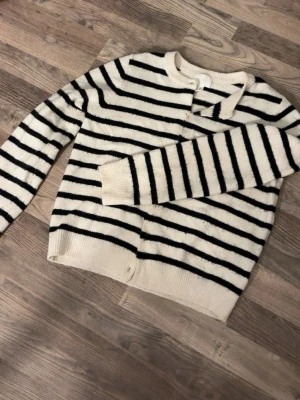 Randig fluffig tröja i vitt och svart - Mysig tröja med svarta horisontella ränder på vit botten. Tröjan är fluffig, har rund halsringning och långa ärmar. Perfekt för dig som gillar en enkel men trendig look med lite extra mjuk känsla.