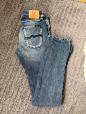 Slim fit jeans från Nudie Jeans - Slim Kim 27/34 Nudie Jeans i färgen indigo on black. Snygg passform som sitter tight längs benen. Perfekt för dig som gillar en modern och stilren look.