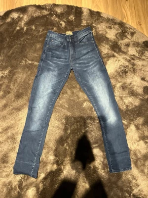 Blå slim fit jeans med slitningar - Snygga blå slim fit jeans med lätt slitna detaljer och klassisk femficksdesign. Jeansen har normalhög midja och smala ben. Materialet ser ut att vara stretchigt denim för extra komfort. Perfekta för en trendig och avslappnad look. 27/30