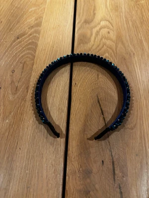 Mörkblått diadem med glittrande stenar - Snyggt mörkblått diadem dekorerat med glittrande, facetterade stenar som ger en lyxig känsla. Diademet har en klassisk form och är täckt med små pärlor som reflekterar ljuset. Perfekt accessoar för att lyfta din look.