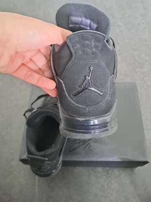 Svarta Air Jordan 4 sneakers - Säljer ett par helsvarta Air Jordan 4 sneakers med mockaliknande ovandel, meshpaneler på sidorna och klassisk Jumpman-logga på hälen. Skorna har en robust sula och coola detaljer som gör dem till ett måste för alla sneakerheads.