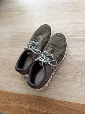 Grågröna sneakers med vit sula on cloud - Snygga sneakers i grågrönt meshmaterial med vita detaljer och unik, segmenterad vit sula. Skorna har lågt skaft och ljusgrå snörning. Perfekta för dig som gillar sportig och modern stil.