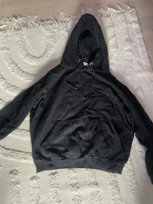 Svart hoodie från Studio Total - Säljer en svart hoodie från Studio Total i storlek S. Hoodien har en stor huva med dragsko, magficka och ribbade muddar vid ärmar och nederkant. Perfekt för en avslappnad och stilren look. Materialet är mjukt och bekvämt, troligen bomullsblandning.