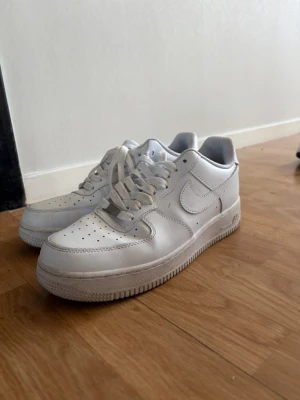 Nike Air Force 1 - Klassiska vita Nike Air Force 1 sneakers i lågt utförande. Skorna är tillverkade i läder med perforerad tåbox för ventilation, vit sula och ikonisk Swoosh på sidan. Passar perfekt till streetwear och har en tidlös look. Skulle behöva tvättas