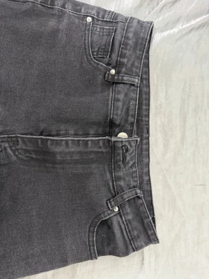 Svarta raka jeans med rå kant/ för dam - Säljer ett par svarta jeans med raka ben och råa, avklippta benslut. Jeansen har klassisk femficksmodell, bälteshällor och silverfärgade nitar. Materialet är denim i bomull med en något tvättad look. Perfekta för en avslappnad och trendig stil.