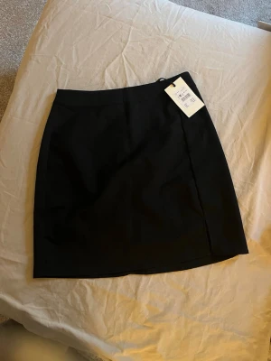 Svart kortkjol i enkel design - Säljer en svart kortkjol med stilren och enkel design. Kjolen har rak passform och är perfekt att matcha med olika toppar för en trendig look. Materialet känns mjukt och bekvämt mot huden.