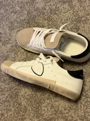 Vita philippe model - Snygga sneakers i vitt skinn med beige mocka på tån och tungan. Skon har vita snören, svart detalj på hälen och en unik sydd patch på sidan. Sulan är vit med en något smutsad look. Perfekta för en trendig och avslappnad stil.