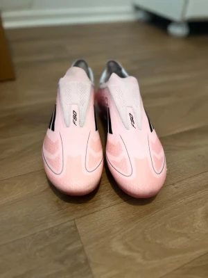 Rosa Adidas F50 fotbollsskor - Säljer ett par rosa Adidas F50 fotbollsskor med svarta detaljer och låg profil. Skorna har en strömlinjeformad design och fasta dobbar för bra grepp på planen. Tillverkade i syntetmaterial för lätt känsla och snabbhet. Perfekta för dig som vill sticka ut på fotbollsplanen.