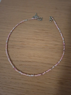 Rosa och vita pärlhalsband - Sött halsband med små pärlor i rosa, vitt och några silverfärgade detaljer. Halsbandet har en tunn och enkel design med metallspänne. Perfekt för att addera en färgklick till din outfit.