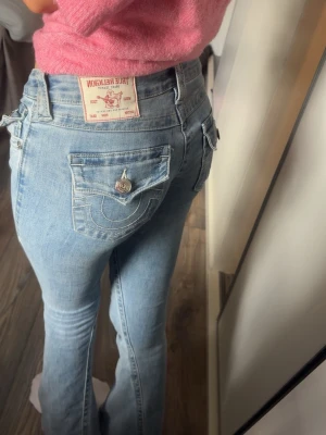 Ljusblå bootcut jeans True Religion - Säljer ett par ljusblå bootcut jeans från True Religion med ikoniska sömmar och ficklock bak. Jeansen har låg midja, knappgylf och detaljerade bakfickor med knapp. Klassisk denim-look i mjukt bomullsmaterial.