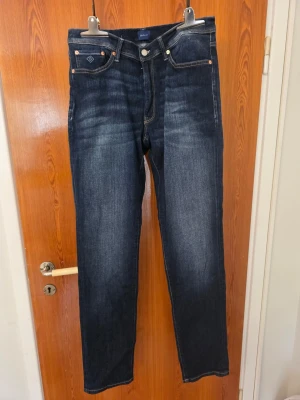 Mörkblå jeans från GANT - Snygga mörkblå jeans från GANT med klassisk femficksdesign och kontrastsömmar. Jeansen har raka ben och subtila slitningar framtill för en cool look. Perfekta för dig som gillar stilrena och tidlösa jeans.