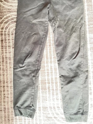 Grå mjukisbyxor från Name It - Mysiga grå mjukisbyxor från Name It med ribbade muddar vid benslut och midja. Tillverkade i mjukt material som känns skönt mot huden. Perfekta för chill dagar hemma eller när du vill ha det extra bekvämt.