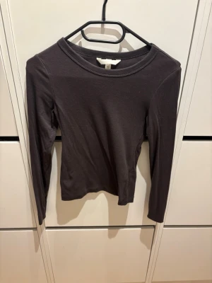 Mörkbrun långärmad topp från H&M - En enkel och stilren mörkbrun långärmad topp från H&M. Modellen är figurnära med rund halsringning och tillverkad i mjukt bomullsmaterial. Perfekt att matcha med jeans eller kjol för en clean look. Ny utan prislapp endast testad. 