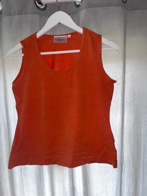 Orange linnetopp från Indiska - Snygg orange linnetopp från Indiska i mjuk bomull. Toppen är ärmlös med rundad halsringning och har en enkel, clean look som passar perfekt till jeans eller kjol. Perfekt för varma dagar och enkel att styla med accessoarer.
