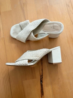 Beiga slip-in klackar från H&M - Säljer ett par beiga slip-in klackskor från H&M med korslagda, flätade band i tyg och öppen tå. Väldigt bekväma klackar, kunnat gå långt i dem. Finns tecken på användning på ex sulan, men absolut inget som syns vid användning. Öppen för prisförhandling🥰🙌