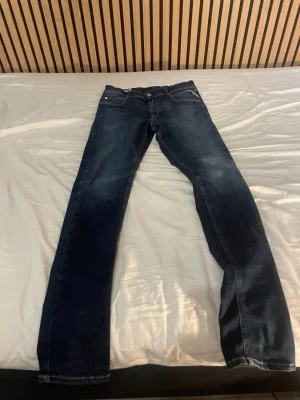 Mörkblå replay jeans  - Säljer ett par mörkblå replay jeans med raka ben och klassisk femficksmodell. Jeansen har snygga slitningar och kontrastsömmar. Perfekta för dig som gillar en enkel och tidlös stil. Materialet är denim i bomull. Priset är ej hugget i sten och går att diskutera.
