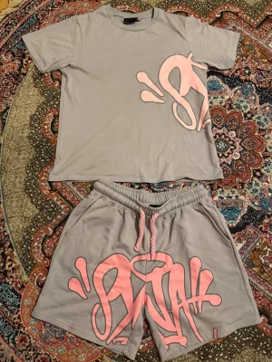 Syna World Grey - Säljer ett matchande set från Syna World i grått med rosa graffititryck och snörning. Använd ett par gånger