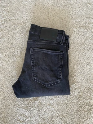 Svarta slim/glen jeans med stretch - Snygga svarta slim/glen jeans från Jack and Jones med lätt tvättad look och klassiska fem fickor. Jeansen har hög midja och smal passform hela vägen ner. Tillverkade i stretchigt material för extra komfort. Perfekta för en trendig och avslappnad stil.