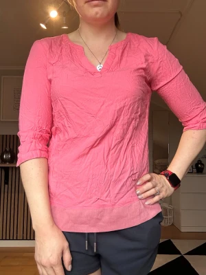 Rosa blus från Tom Tailor - Snygg rosa blus från Tom Tailor med v-ringning och trekvartsärm. Tillverkad i ett lätt och luftigt material som passar perfekt till vår och sommar. Enkel design med bredare kant nedtill för en avslappnad look.