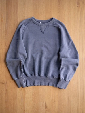 Blå Vintage sweatshirt med raglanärm - En stilren blå sweatshirt med raglanärmar och ribbade muddar vid ärmslut och nederkant. Tröjan har en klassisk rund halsringning med V-detalj framtill. Perfekt för en avslappnad och trendig look.