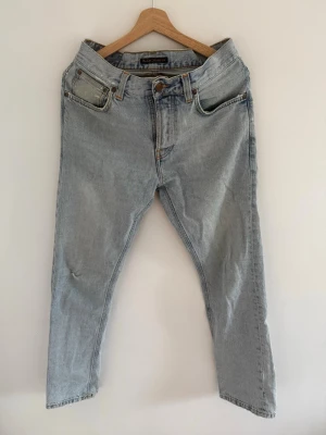 Ljusblå jeans Nudie Jeans - Säljer ett par ljusblå jeans från Nudie Jeans med rak passform och klassisk femficksdesign. Jeansen har detaljerade bakfickor med Nudie Jeans signaturbrodyr. Tillverkade i denim av bomull.