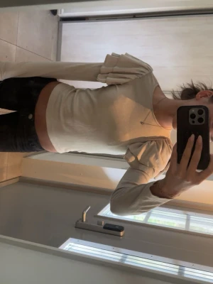 Beige croppad topp med volangärm - Trendig beige croppad topp med långa ärmar och volangdetaljer på axlarna. Sitter tight och har en stilren, enkel design som passar perfekt till jeans eller kjol. Perfekt för dig som vill ha en unik och snygg topp i garderoben.