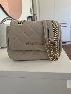 Beige quiltad handväska Valentino - Snygg beige handväska från Mario Valentino med quiltat mönster och guldfärgade kedjor. Köpt på zalando för 1345kr och använd bara 2-3 gånger så väskan är i perfekt skick.