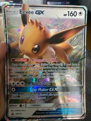 Pokémonkort Eevee GX SM175 Promo - Säljer ett Pokémonkort med Eevee GX från Sun & Moon-serien, SM175 Promo. Kortet har en holografisk yta och färgstark design med Eevee i fokus. Text och effekter på engelska. Perfekt för samlare eller Pokémonfans.