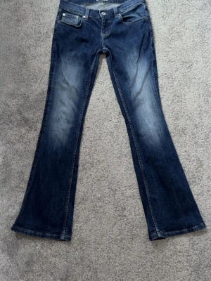 Mörkblå bootcut jeans med brodering på bakfickorna - Ett par jeans i lätt stretchig denim. Jeansen har låg midja med lätt utsvängda benslut. Midjemått: 38 cm. Insida ben: 78 cm