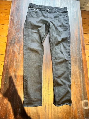 Svarta skinny jeans med fem fickor - Säljer ett par svarta skinny jeans med klassisk femficksmodell och smal passform. Jeansen har bälteshällor, knappgylf och raka ben. Materialet är stretchigt denim som sitter snyggt och bekvämt. Perfekta till en avslappnad look.