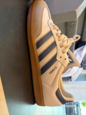 Adidas Samba vita, blå och grå sneakers - Säljer ett par klassiska Adidas Samba sneakers i vitt och grått med mörkblå ränder och detaljer. Använda endast (EN) gång. Blev för het och hade dem på mig en utekväll, men de var för små. Obsavera att endast toppen av skorna är lite smutsiga, resten är helt rena. Köpta för 1500, pris kan diskuteras!