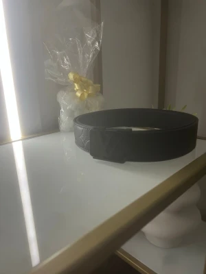 Svart bälte med L och V 120cm - Snyggt svart bälte i skinn med präglad logga och matchande svart spänne. Bältet har en stilren och modern look som passar till många olika outfits. Perfekt accessoar för dig som vill ha en clean och trendig stil.