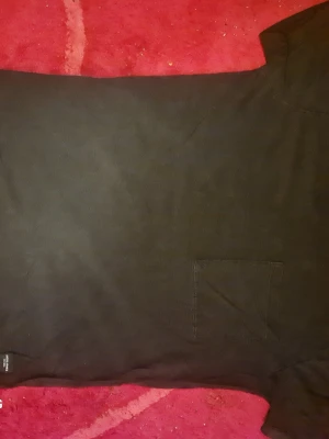 Svart t-shirt med bröstficka - En enkel svart t-shirt med rund hals och en praktisk bröstficka på vänster sida. Tillverkad i mjukt bomullstyg som känns skönt mot huden. Perfekt basplagg för alla tillfällen och lätt att matcha med andra kläder.