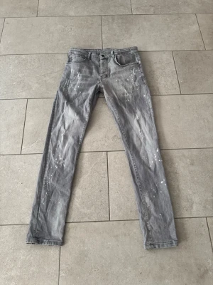 Grå slim fit jeans från desquarede - Säljer ett par grå slim fit jeans från desquaered med coola vita färgstänk och slitningar. Klassisk femficksmodell med bälteshällor och knappgylf. Perfekta för dig som gillar en avslappnad och trendig stil.