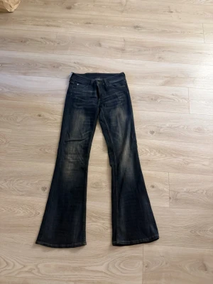 Mörkblå bootcut jeans - Snygga mörkblå bootcut jeans med lätt slitning på låren och knäna. Klassisk femficksmodell och låg midja. Jeansen har en utsvängd passform nertill och är perfekta för en avslappnad stil.