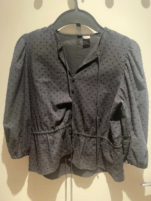 Svart blus  - Svart blus med puffärmar, knappar och snörning uppe vid halsen och vid midjan💕