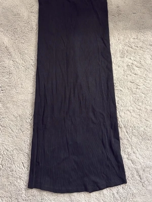 Svart långkjol med slits - En svart långkjol i ribbad bomull med diskret slits på sidan. Kjolen har en enkel och stilren design som passar till många olika looks. Perfekt för dig som gillar minimalistisk stil och vill ha en bekväm kjol med lite edge.