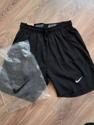 Nike shorts - Säljer ett par svarta Nike shorts med elastisk midja och snörning. Shortsen har en klassisk passform och är tillverkade i ett lätt och bekvämt material, perfekt för träning eller chill. Nike-logga syns tydligt på ena benet och i midjan.