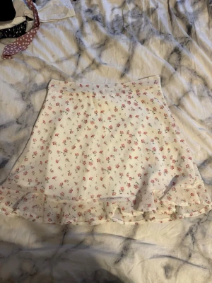 Vit blommig kjol från SHEIN - Supersöt vit kortkjol från SHEIN med små rosa blommor och volangkant längst ner. Kjolen har en diskret dragkedja i sidan och är perfekt för vår och sommar. Lätt och luftig känsla, passar till allt från sneakers till sandaler.