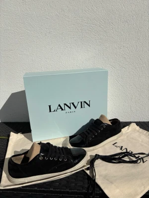Svarta skor från Lanvin - Snygga svarta sneakers från Lanvin med blank tå i lack och ovandel i mocka. Skorna har vita sulor, svarta skosnören och beige innersula. Kommer med originalpåse och box. Perfekta för dig som vill ha en clean och lyxig look.