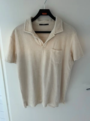 Beige frottéskjorta med krage - Säljer en beige skjorta i mjuk frotté med korta ärmar och öppen krage. Skjortan har en bröstficka och avslappnad passform, perfekt för sommarens chill dagar.