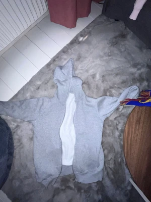 Ljusgrå hoodie med dragkedja - En basic ljusgrå hoodie med dragkedja framtill och två fickor. Hoodien har en klassisk huva och är gjord i mjukt sweatshirtmaterial. Perfekt för chill dagar eller när du vill ha något bekvämt och enkelt.