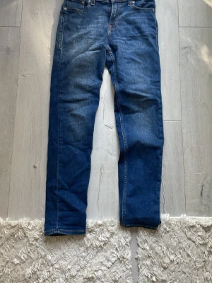 Blå jeans från Jack & Jones - Snygga blå jeans från Jack & Jones med klassisk femficksdesign och raka ben. Jeansen har en djupblå tvätt med lätt slitning och är tillverkade i ett mjukt denimtyg. Perfekta för en avslappnad och trendig look. 