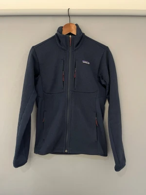 Mörkblå fleecejacka från Patagonia - Mörkblå fleecejacka från Patagonia. Storlek XS. Perfekt att slänga på direkt över en t shirt och funkar att ha året runt. Både väldigt varm men även stilren