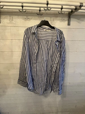 Randig blåvit skjorta från H&M - Snygg randig skjorta från H&M i blått och vitt. Skjortan har långa ärmar, klassisk krage och knappar framtill. Tillverkad i ett lätt och bekvämt bomullsmaterial, perfekt för en avslappnad stil.