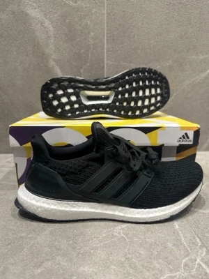 Adidas Ultraboost svarta sneakers - Svarta Adidas Ultraboost sneakers med stickad ovandel, vita Boost-sulor och svarta detaljer. Skorna har klassiska tre ränder på sidan och en flexibel, bekväm passform. Perfekta för dig som gillar stilrena och sportiga sneakers.