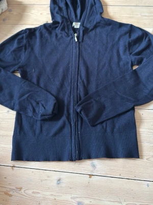Mörkblå kofta gina Young  - En enkel svart hoodie med dragkedja framtill och huva. Tillverkad i mjukt material och har långa ärmar samt ribbade muddar vid ärmslut och nederkant. Perfekt för en avslappnad stil och lätt att matcha med andra plagg.
